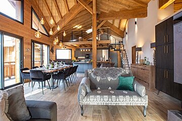 Cozy modern chalet interior with high wooden ceilings, hanging bulb lights, a dining area, and stylish rustic furniture.