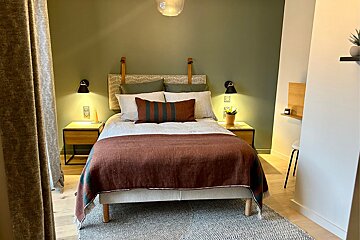 A warm, modern bedroom with an olive green accent wall, a bed featuring brown and striped bedding, and illuminated wooden nightstands.