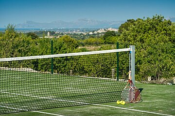 A patio with wicker furniture and umbrellas with a tennis court in the background