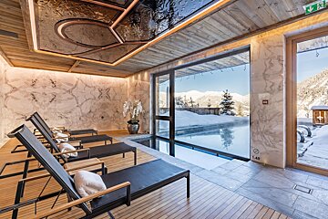 Luxurious indoor pool area with lounge chairs, marble walls, and a stunning snowy mountain view through large windows.