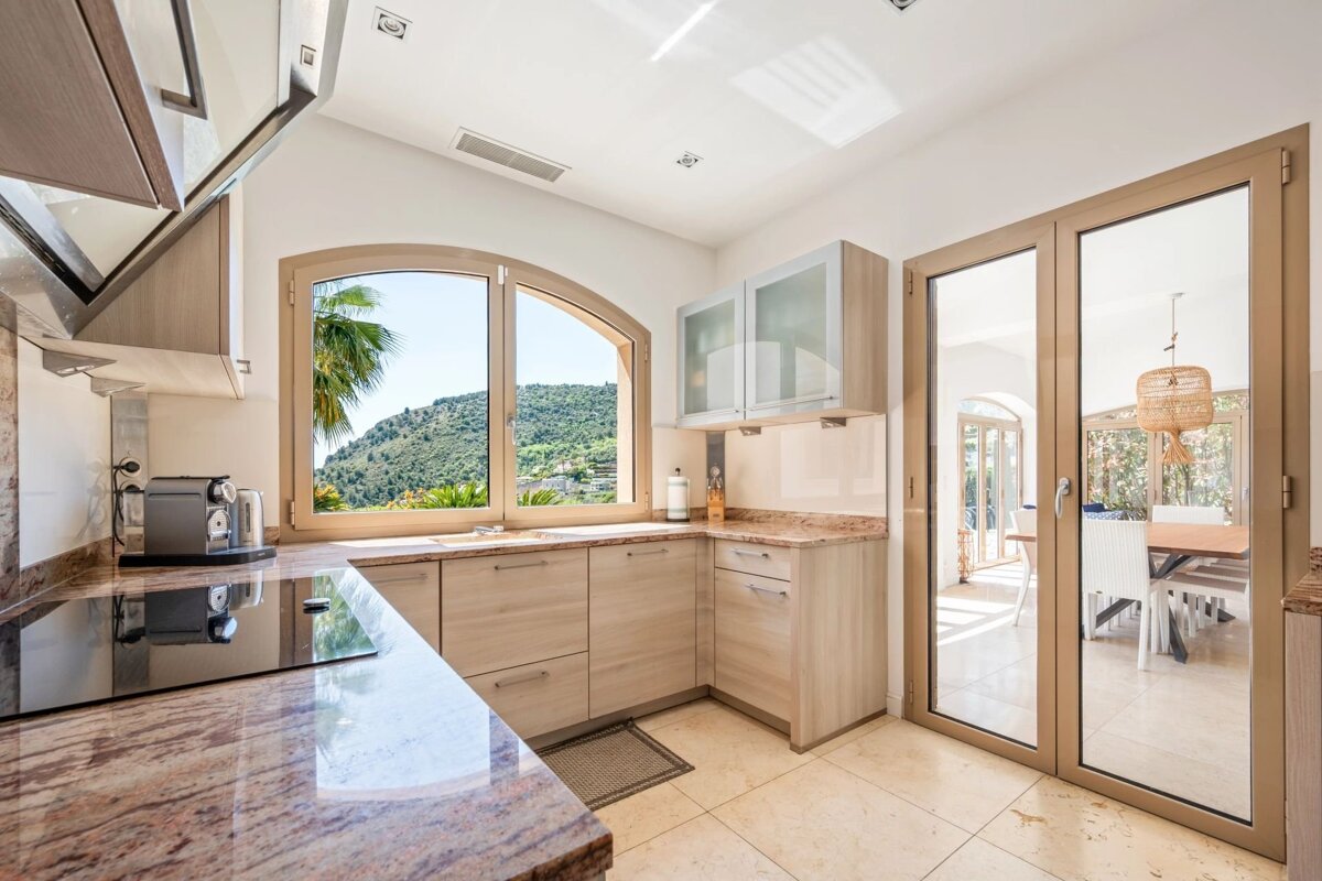 Bright, modern kitchen featuring light wood cabinets, granite countertops, and an arched window overlooking scenic hills.