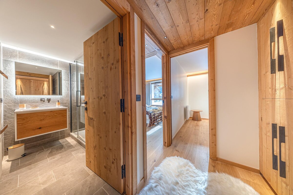 Modern chalet hallway with light wood panels, a fluffy white rug, and an open bathroom with a floating vanity on the left.