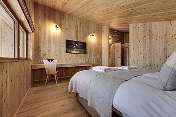 Warm, rustic bedroom completely paneled in light wood, featuring a cozy bed, a desk and chair, and a wall-mounted TV.