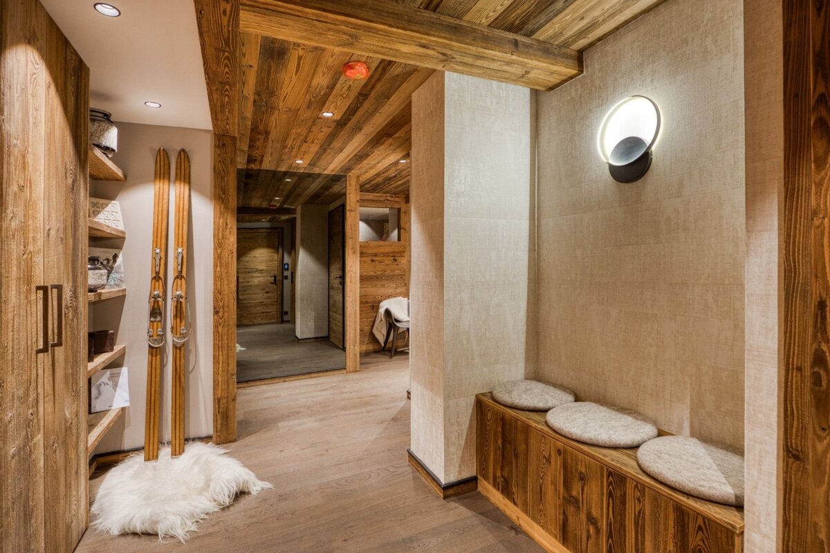Cozy, rustic chalet hallway with wooden accents, vintage skis on a fur rug, a wooden bench, and warm lighting.