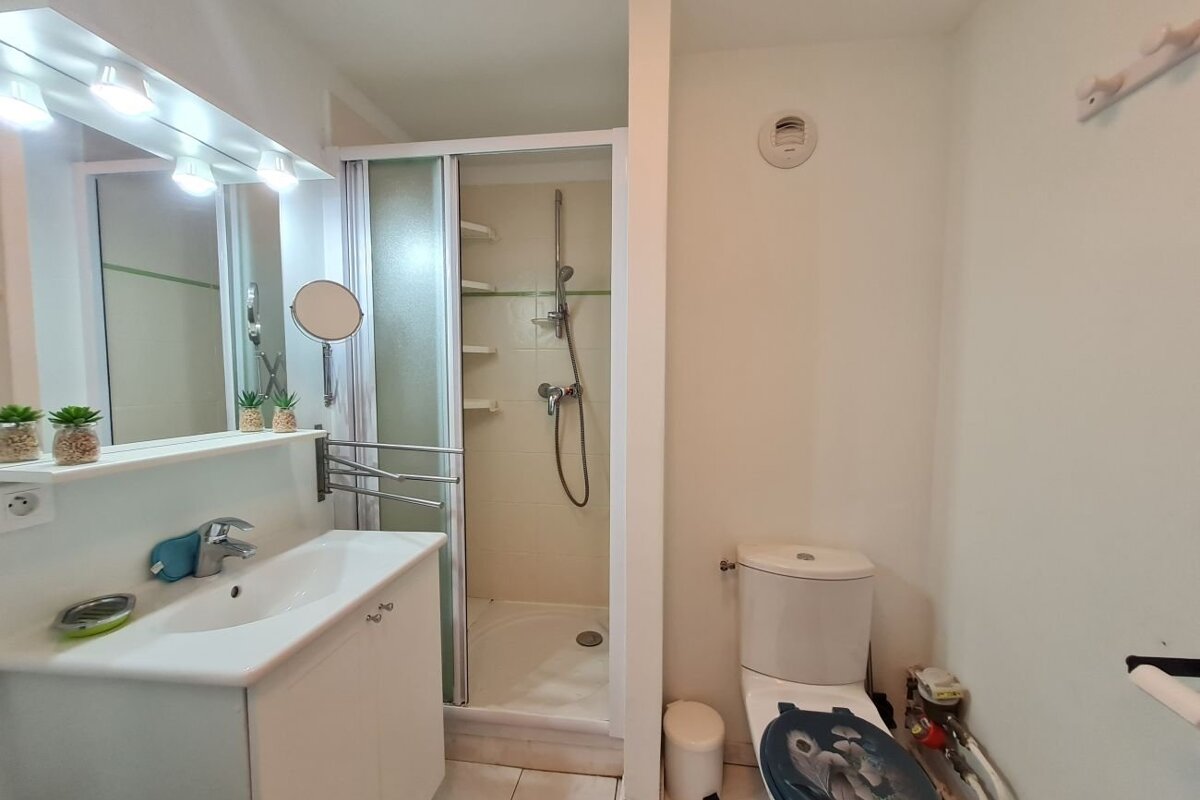 A compact white bathroom featuring a sink vanity with a mirror, a standing glass shower stall, and a toilet.