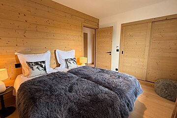 Cozy chalet bedroom featuring wood-paneled walls and a bed with a plush grey fur blanket.