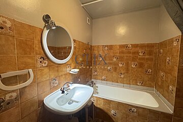 Small bathroom with brown patterned tiles, a white sink with an oval mirror above it, and a built-in bathtub.