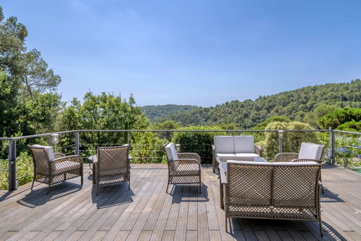 An outdoor wooden deck with wicker patio furniture overlooking lush green hills under a clear blue sky.