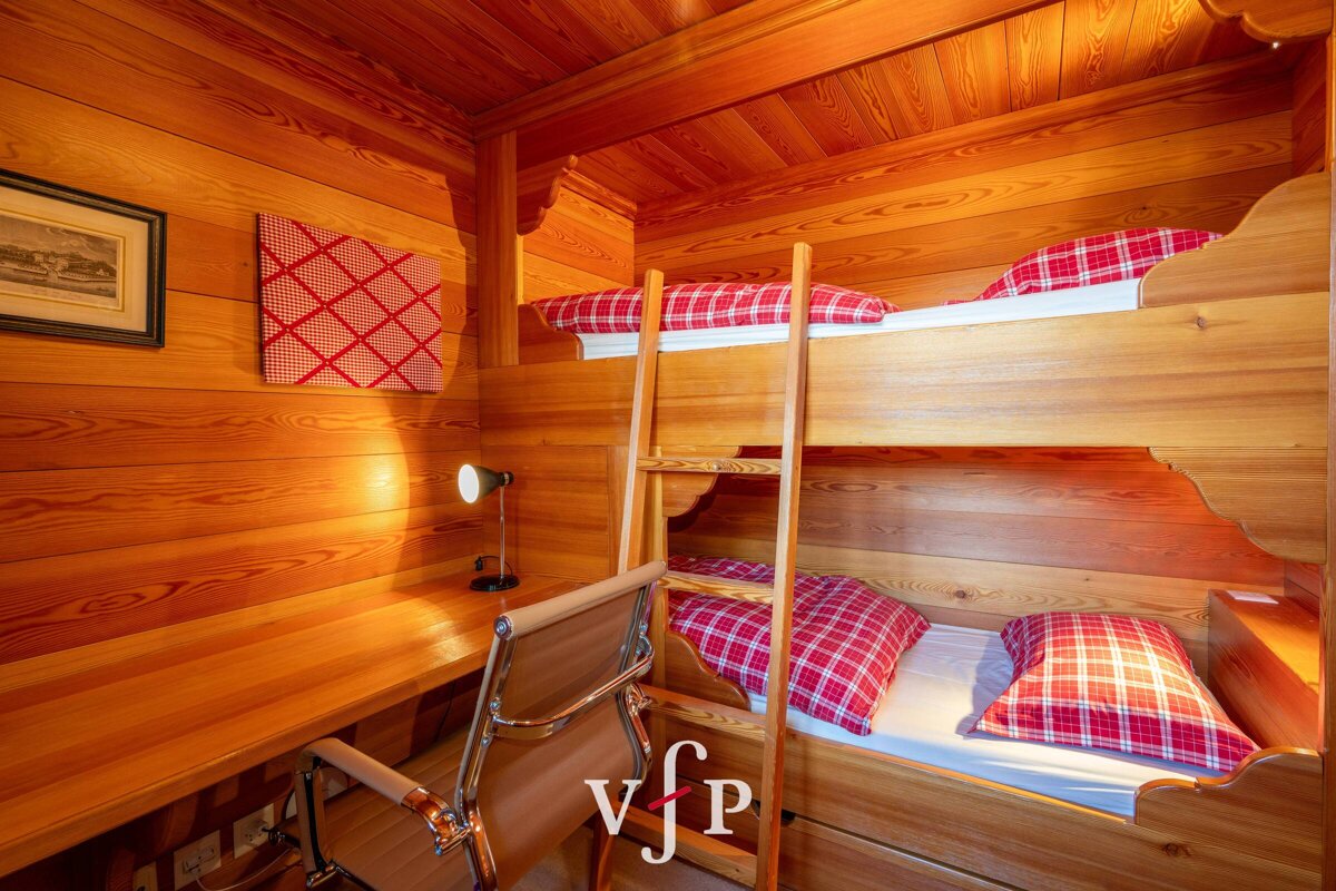 A wooden bunk bed with red plaid sheets and a vfp logo in the corner