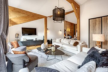 A stylish, modern living room with exposed wooden beams, white sofas, grey armchairs, and contemporary coffee tables.