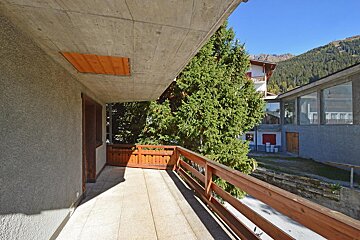 A balcony with a wooden railing and mountains in the background