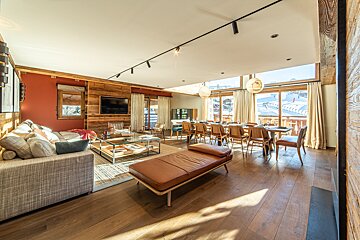 Modern chalet interior featuring a cozy living room, dining area, and large windows overlooking a snowy ski slope.