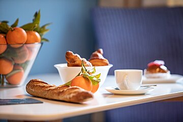 A cup of coffee sits on a table next to a bowl of oranges