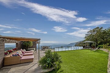 Luxurious terrace with lounge seating on a wooden deck, a green lawn, and a pool overlooking a scenic mountain valley.