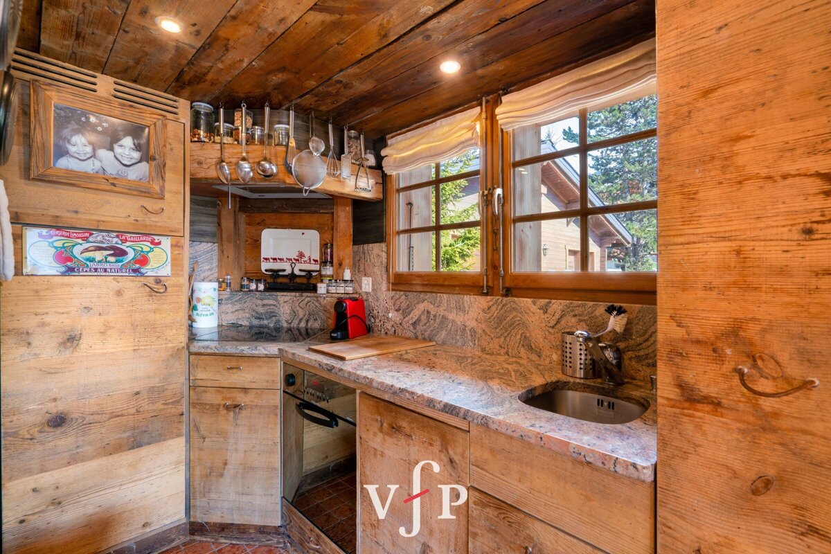 Rustic cabin kitchen with warm wooden cabinets, granite countertops, a small sink, and two windows looking outside.