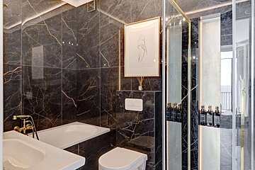 A luxurious bathroom with dark, gold-veined marble walls, featuring a bathtub, toilet, and modern shower. Accent lighting enhances the chic design.