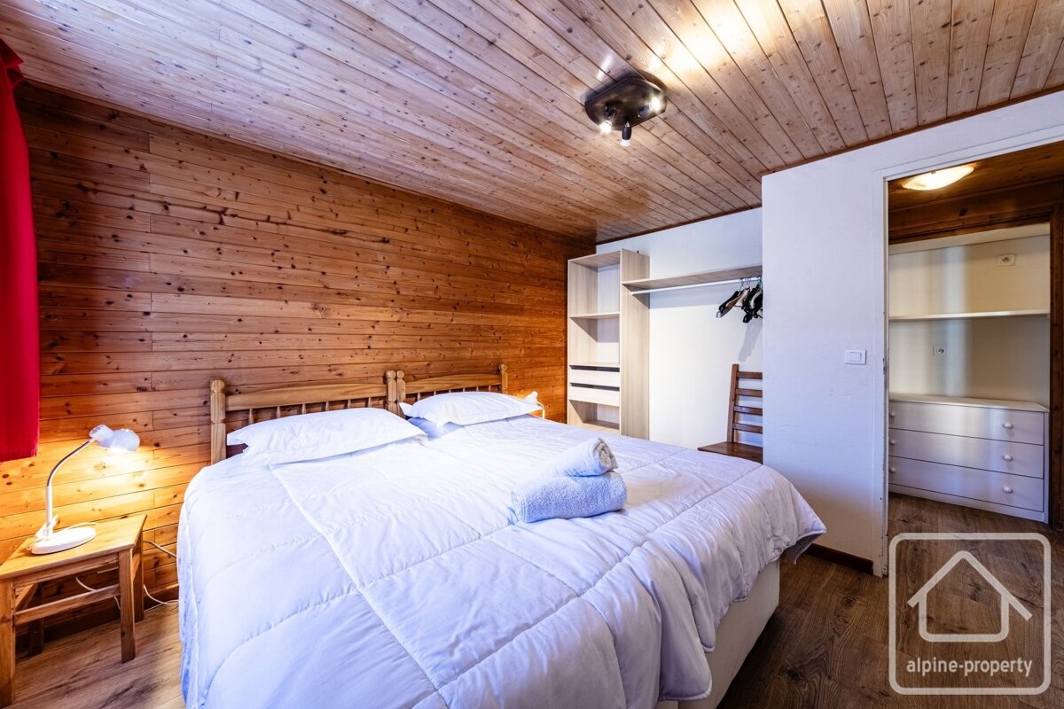 Cozy wood-paneled bedroom with a large bed, white linens, a nightstand with a lamp, and an open wardrobe area.