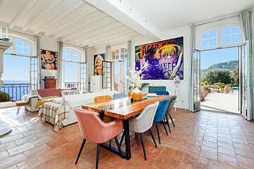 A living room with a dining table and chairs and a large painting on the wall