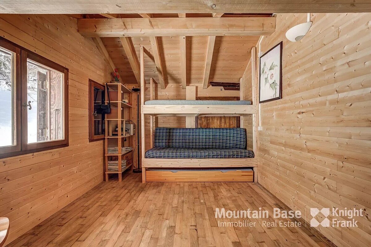 A cozy wooden cabin room with bunk beds, a plaid futon, and a pull-out bed. Natural wood walls, floor, and ceiling beams create a warm, rustic interior.
