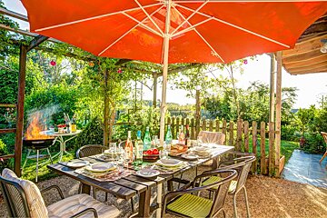 A table and chairs under an orange umbrella in a garden