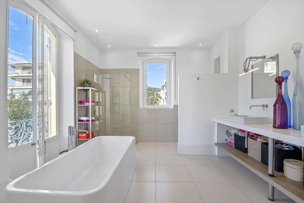 Bright, modern bathroom with a white bathtub, glass shower, sink, and large windows offering an outdoor view.