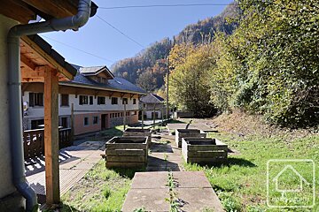 Alpine buildings and wooden planters on a grassy slope, backed by a vibrant autumn mountain under a clear sky.