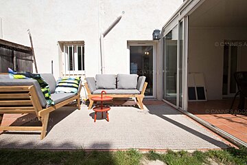 A patio with a couch and a table with the words cannes acco on the bottom