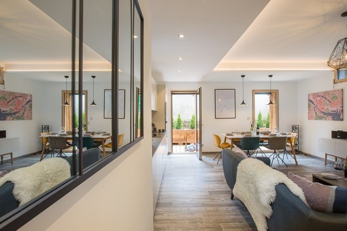 Modern apartment interior with a large mirror wall reflecting a living and dining area, with a glass door opening to a patio.