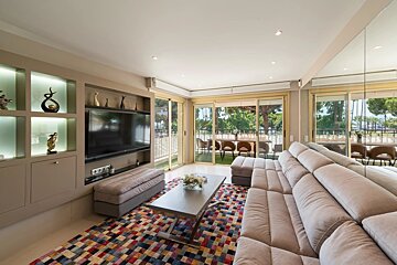 Modern living room with a large sectional sofa, colorful patterned rug, and sliding glass doors opening to a scenic balcony.