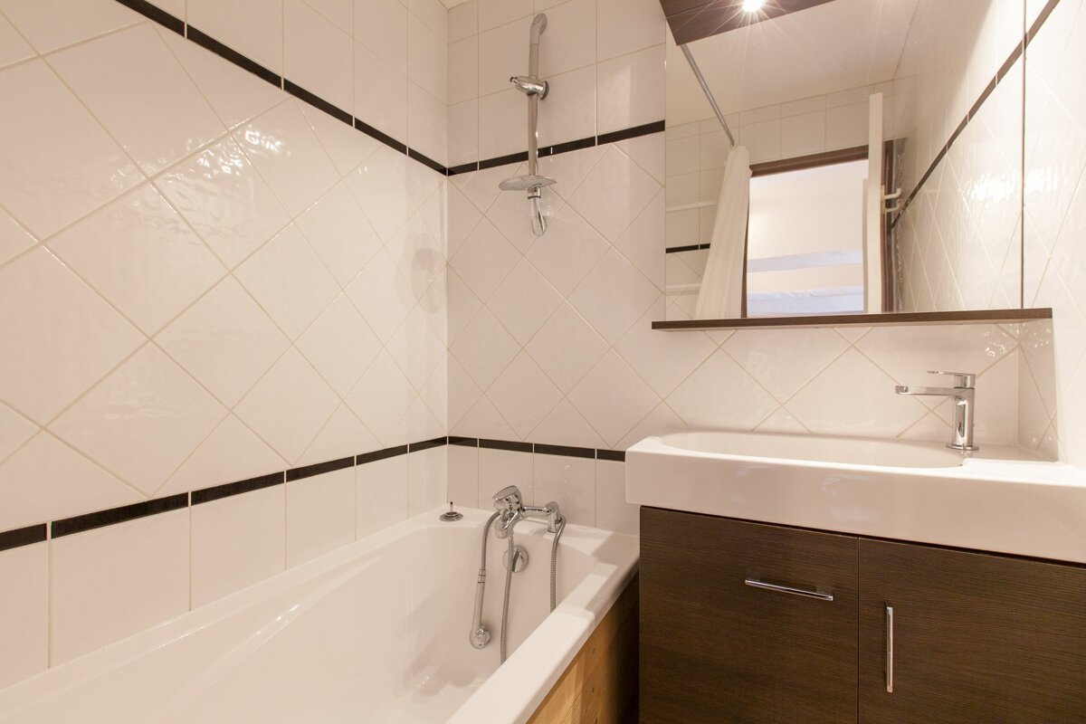A modern bathroom featuring white diamond-tiled walls with black trim, a bathtub with a shower, and a vanity with a sink and mirror.