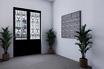 A modern apartment lobby with a black iron door, grey mailboxes, white walls, and three potted green plants.