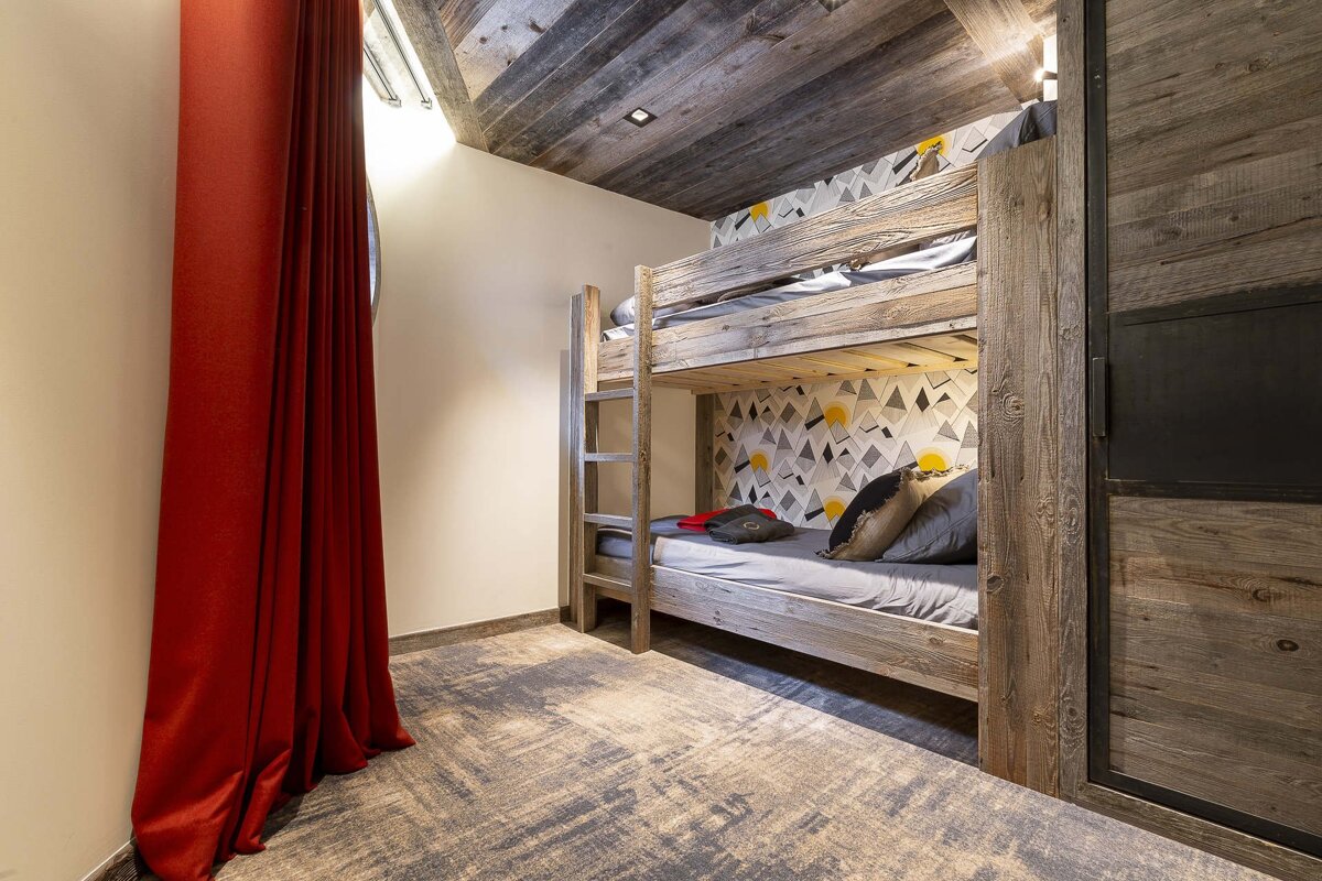 Rustic bedroom featuring wooden bunk beds, a wooden ceiling, patterned wallpaper, and a vibrant red curtain.