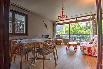 Cozy apartment dining and living room with a red daybed, unique chairs, and sliding glass doors opening to a green balcony view.