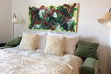 A painting hangs above a bed with pillows