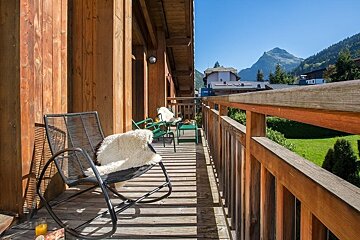 A sunny chalet balcony with a rocking chair and sheepskin throw, overlooking scenic mountain views.