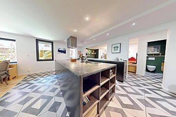 Modern kitchen with a large island, patterned floor tiles, and an open layout connecting to other rooms, including a green-walled bathroom.