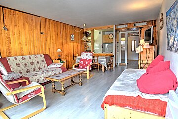 Cozy living room with wood-paneled walls, floral and red sofas, a coffee table, and a dining area in the background.