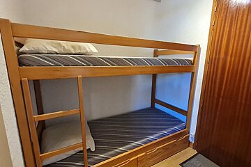 Wooden bunk bed with striped mattresses and white pillows, located next to a closed wooden door.