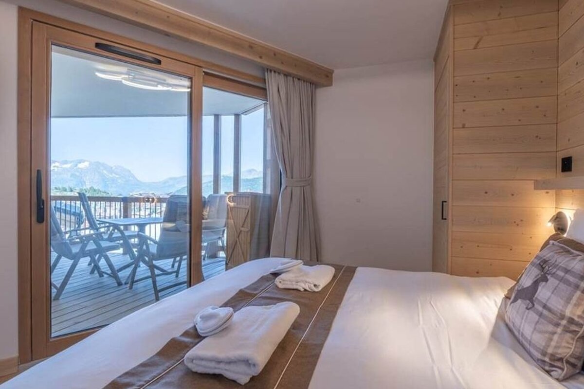 A cozy alpine bedroom with sliding glass doors opening onto a balcony with scenic mountain views.