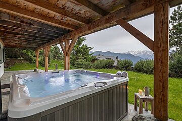 A hot tub under a wooden roof with mountains in the background