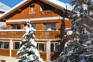A snowy house with a balcony and a tree in front of it