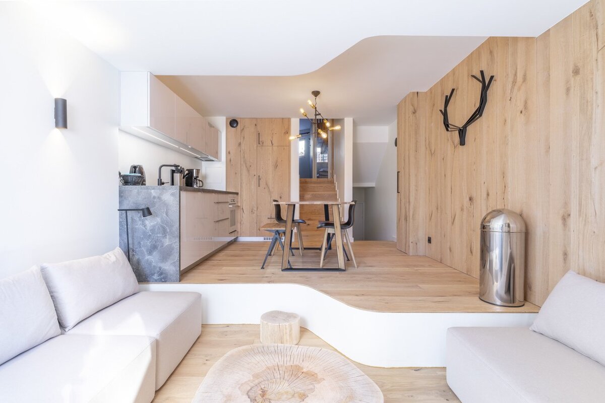 Modern split-level apartment featuring a minimalist living room and a raised kitchen and dining area with warm wood paneling.