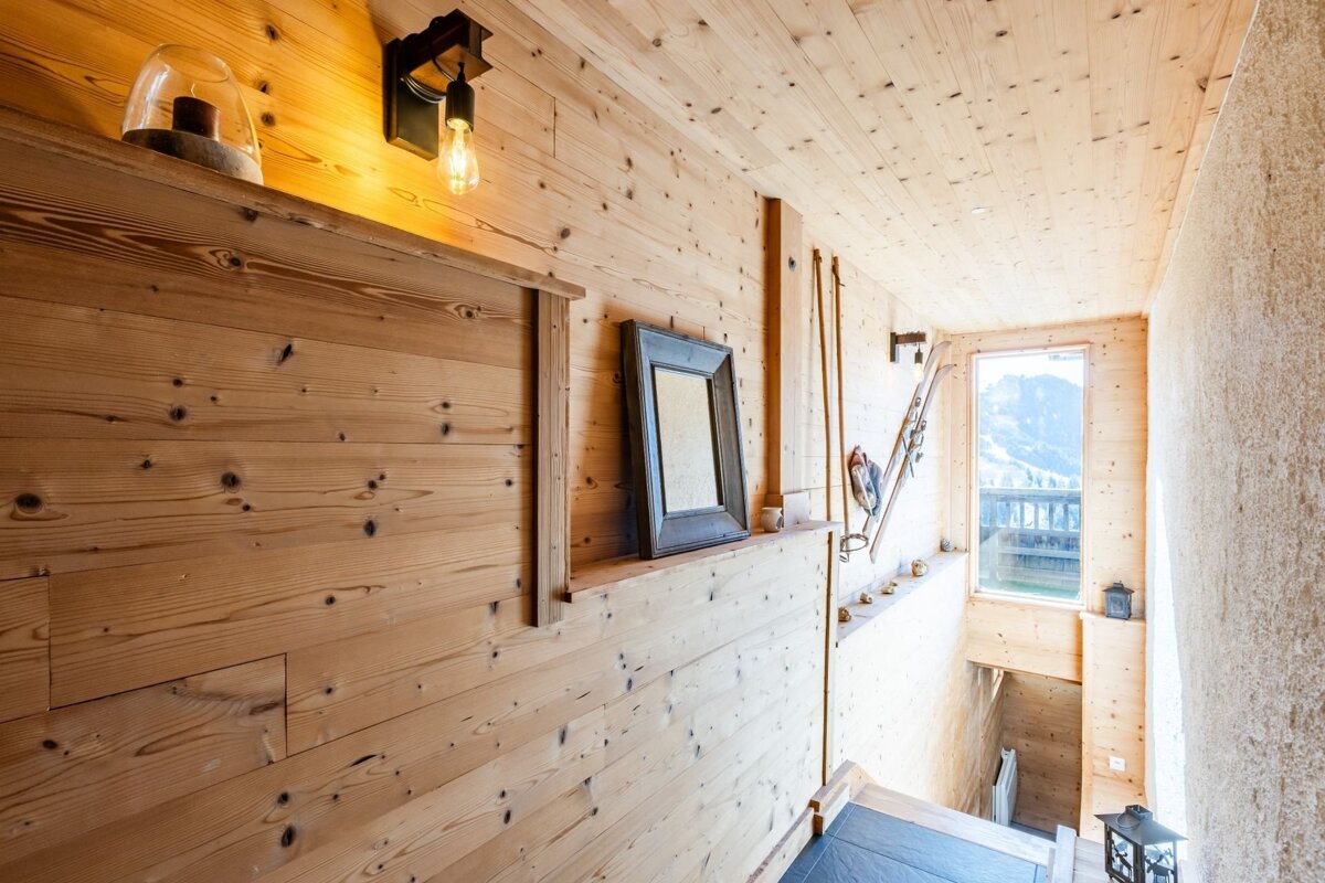 Rustic wood-paneled cabin interior with alpine decor, a glowing wall light, and a window overlooking a snowy mountain view.