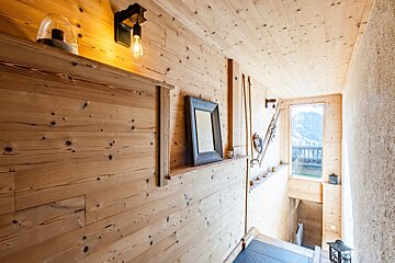 Rustic wood-paneled cabin interior with alpine decor, a glowing wall light, and a window overlooking a snowy mountain view.
