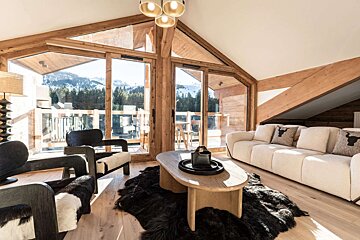 Cozy ski chalet living room with wooden beams, panoramic mountain views, modern rustic decor, cream sofa, and furry rugs.