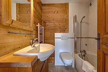 Rustic chalet-style bathroom featuring wood-paneled walls, a white sink, a toilet, and a bathtub.