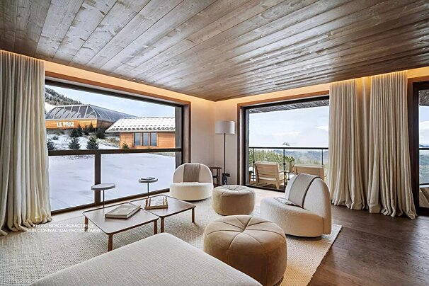 A cozy, modern living room with large windows overlooking a snowy mountain landscape, featuring a wooden ceiling and comfortable seating.