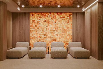 Four plush lounge chairs in a warm spa relaxation room featuring a glowing orange Himalayan salt wall.