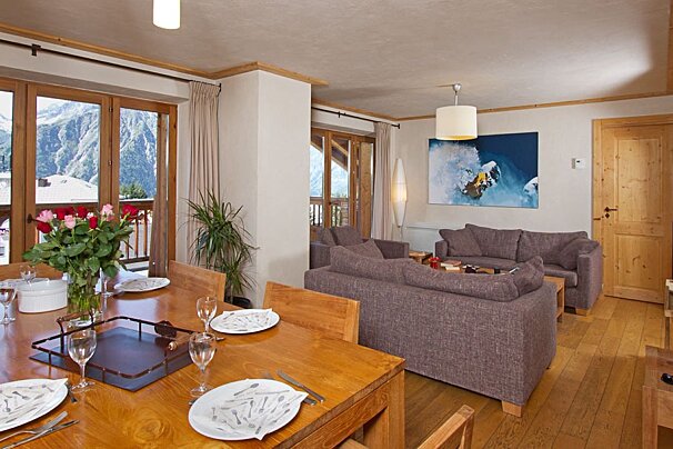 Inviting open-plan living/dining room with wooden furnishings, gray sofas, modern art, and a balcony overlooking mountains.
