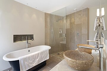 Luxurious bathroom with a black freestanding tub, glass walk-in shower, and dual stone vessel sinks. Neutral colors and recessed lighting.